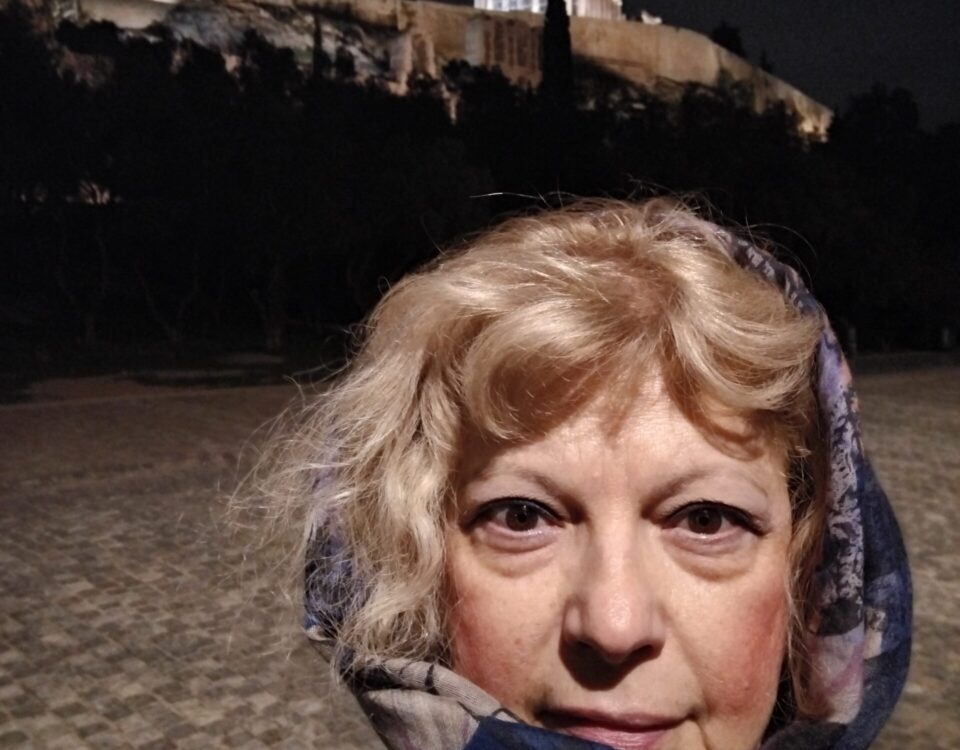 Απεικονίζεται η συγγραφέας Μαρία Μπούκλα μπροστά από τον βράχο της Ακρόπολης